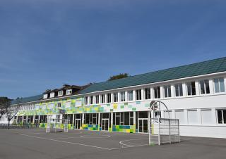 Depuis la cour, vue de la façade d'une école dont le toit est entièrement recouvert de panneaux solaires
