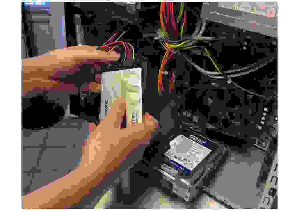 gros plan sur des mains manipulant une carte reliée à des files de couleurs, à l'intérieur de l'unité centrale d'un ordinateur