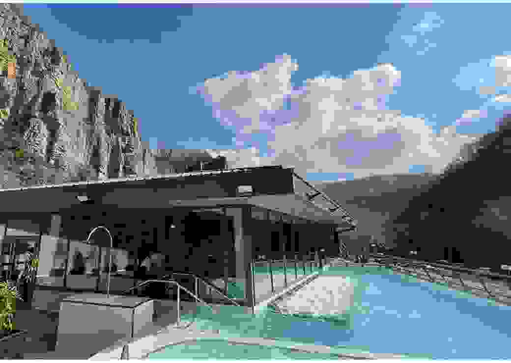 Plan large sur une piscine en plein air, où l'on voit l'eau bouiller. Le batiment moderne attenant est adossé à une falaise