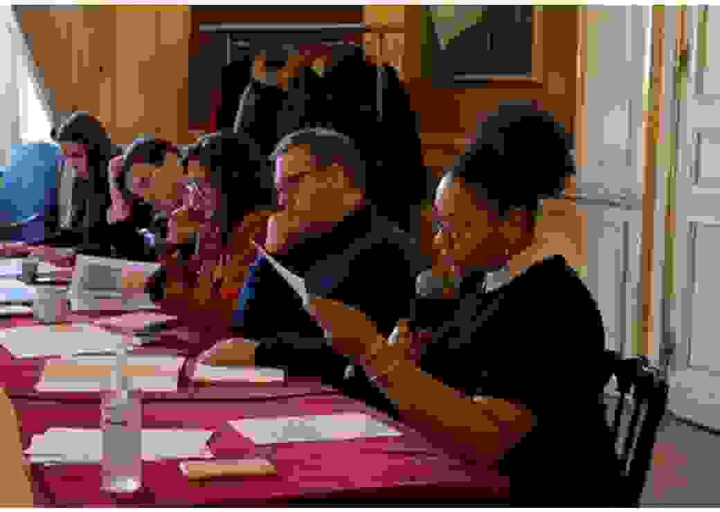5 personnes assises à une table lisent des documents, l'une des personnes parle avec un micro