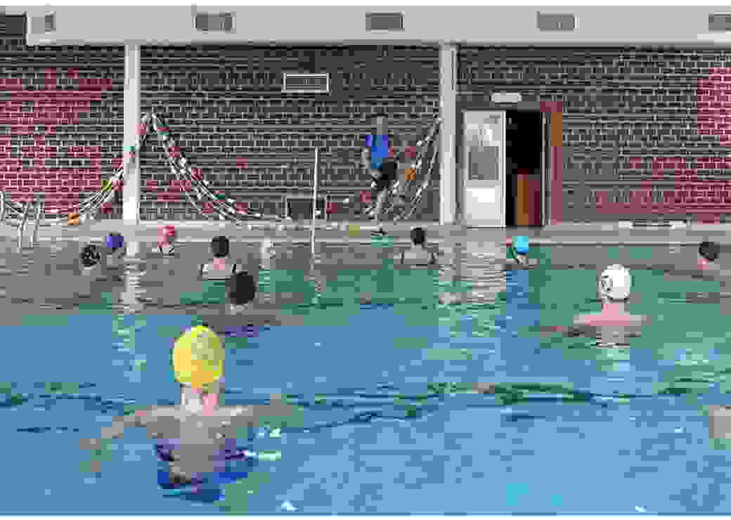 Dans une piscine, un homme montre des mouvements à des personnes immergées et coiffées d'un bonnet de bain