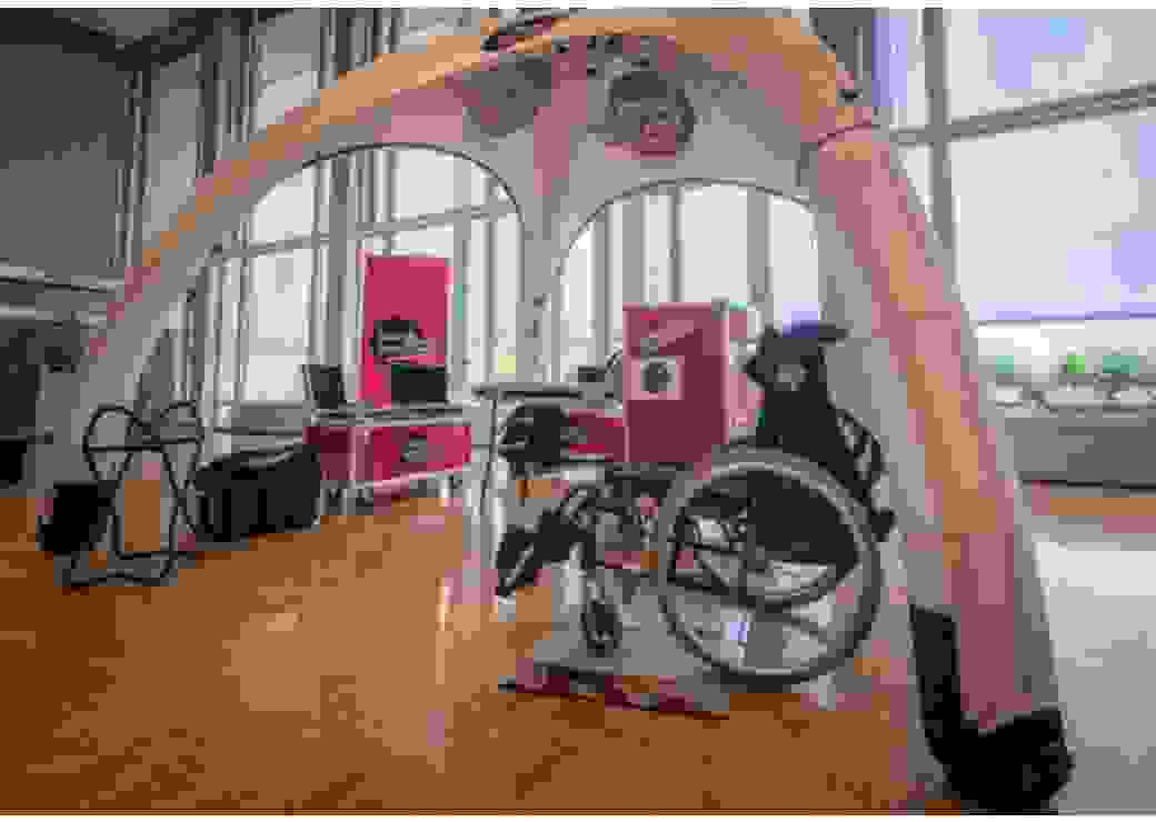 Dans une très grande salle, sous un chapiteau ouverts sur les côtés, sont présentés un fauteuil roulant et des grandes caisses rouges