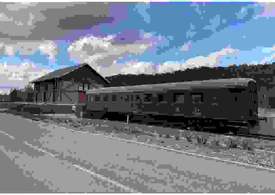 Sur le bord d'une route, un wagon de train ancien et une maison de briques