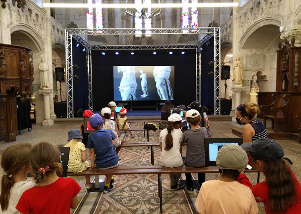 À l'intérieur d'un bâtiment religieux, des enfants regardent sur grand écran des photos d'oeuvres d'art