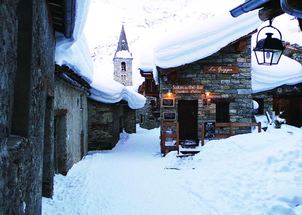 Un village de montagne enneigé, les maisons sont en pierres massives aux toits couverts de neige
