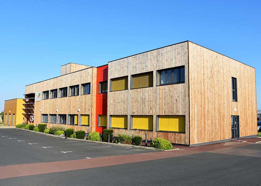 Un bâtiment, parallélépipède rectangle de 2 étages, bardé de bois doré, sur fond de ciel bleu.