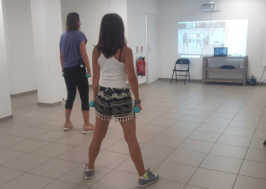 Deux personnes tenant à la main des petite haltères regardent un écran