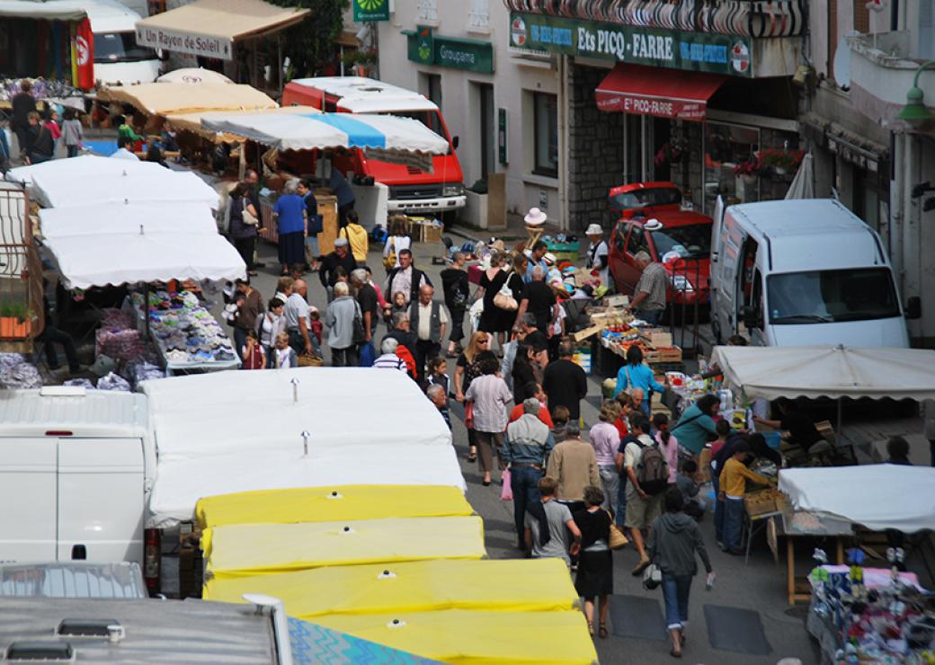 Vue d'en haut d'une rue animée par un marché, avec de la foule et les parasols des marchands