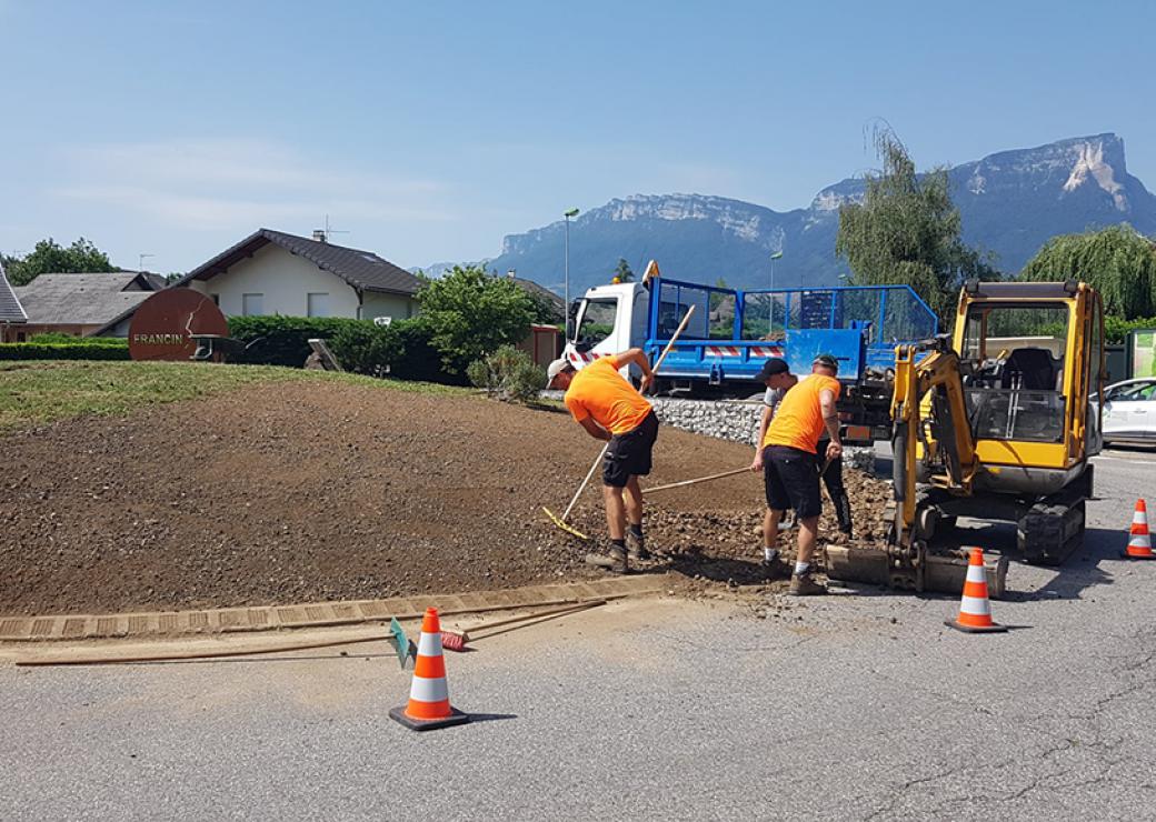 Sur un rond-point, avec une montagne en arrière-plan, trois hommes aménagent une butte de terre