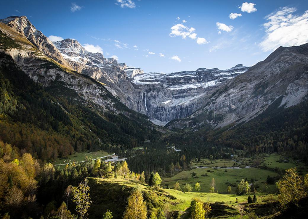 Plan large sur un paysage sauvage de montagne: des sommets enneigés encadrent une vallée verdoyante