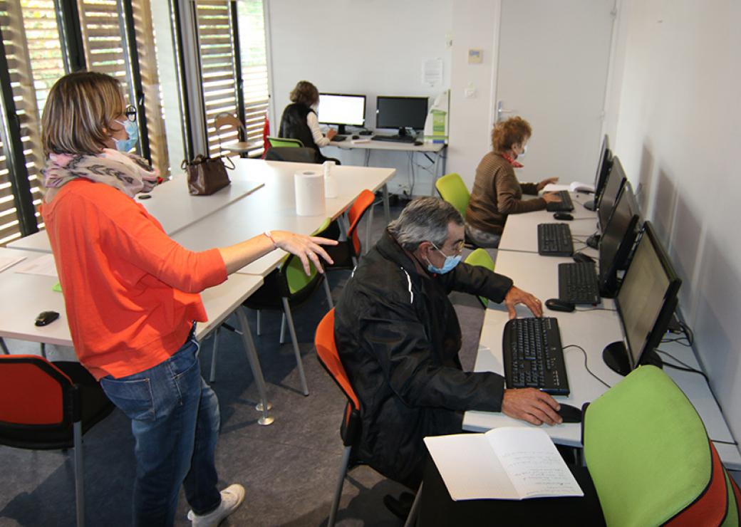Dans une salle, trois personne se tiennent assis devant des ordinateurs tandis qu'une femme debout semble leur donner des instructions