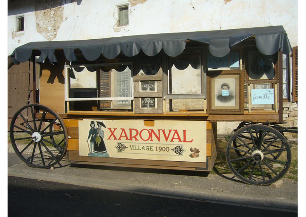 La photo montre une charrette ancienne sur laquelle on peut lire "Xaronval, village 1900"