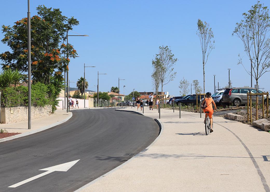 Plan large sur une rue bordée d'un trottoir équipé d'une large piste cyclable surs laquelle circule un vélo