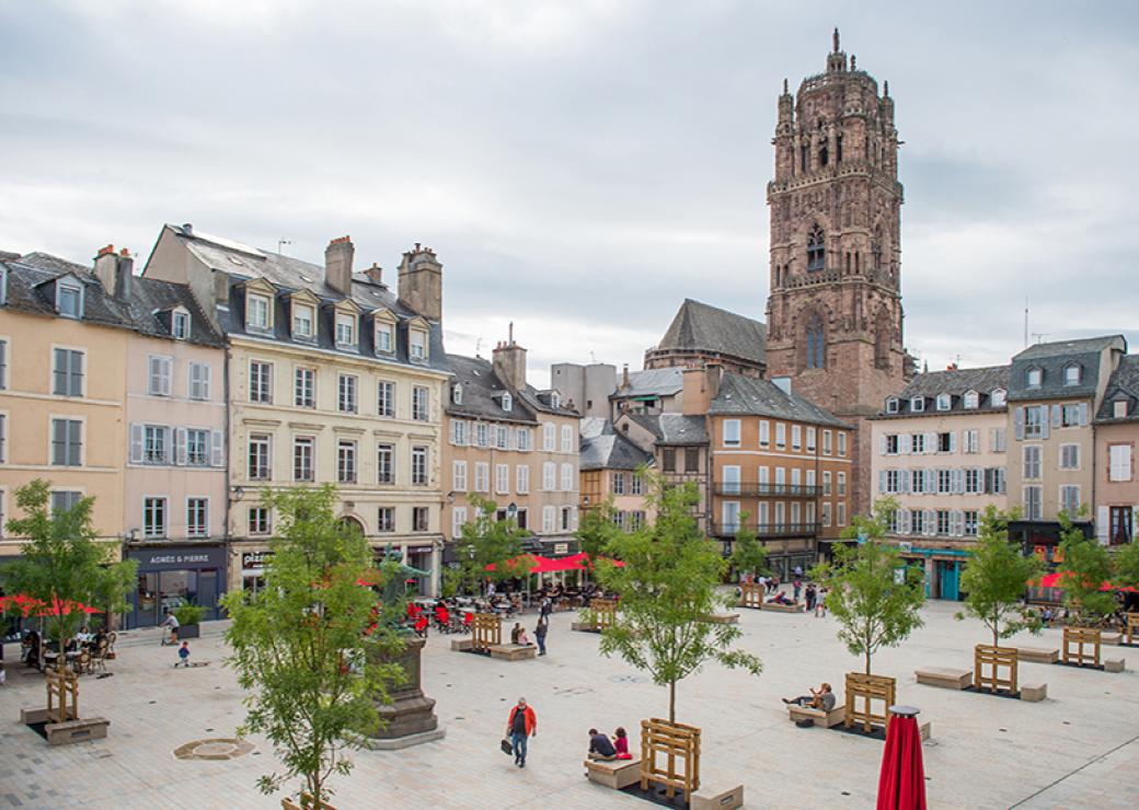 Vue sur un place bordée de bâtiments bourgeois. Dans l'angle, le clocher d'une église. 