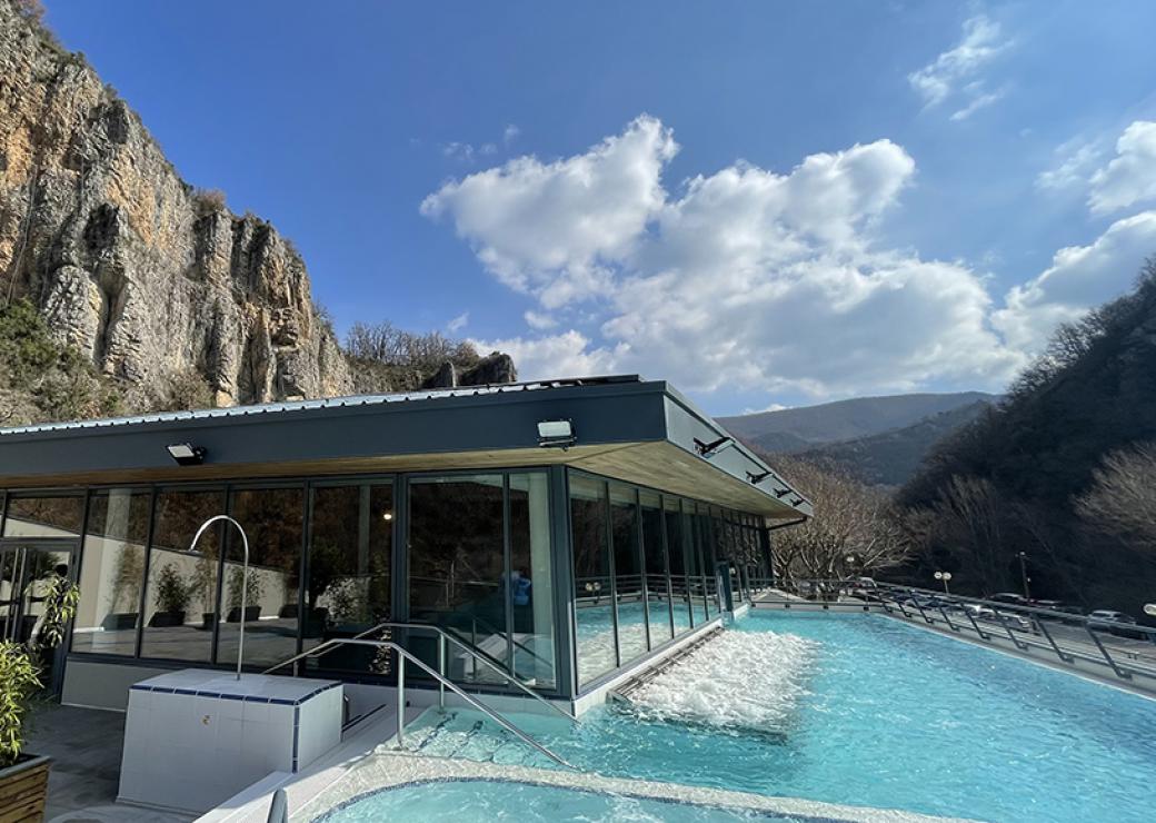 Plan large sur une piscine en plein air, où l'on voit l'eau bouiller. Le batiment moderne attenant est adossé à une falaise