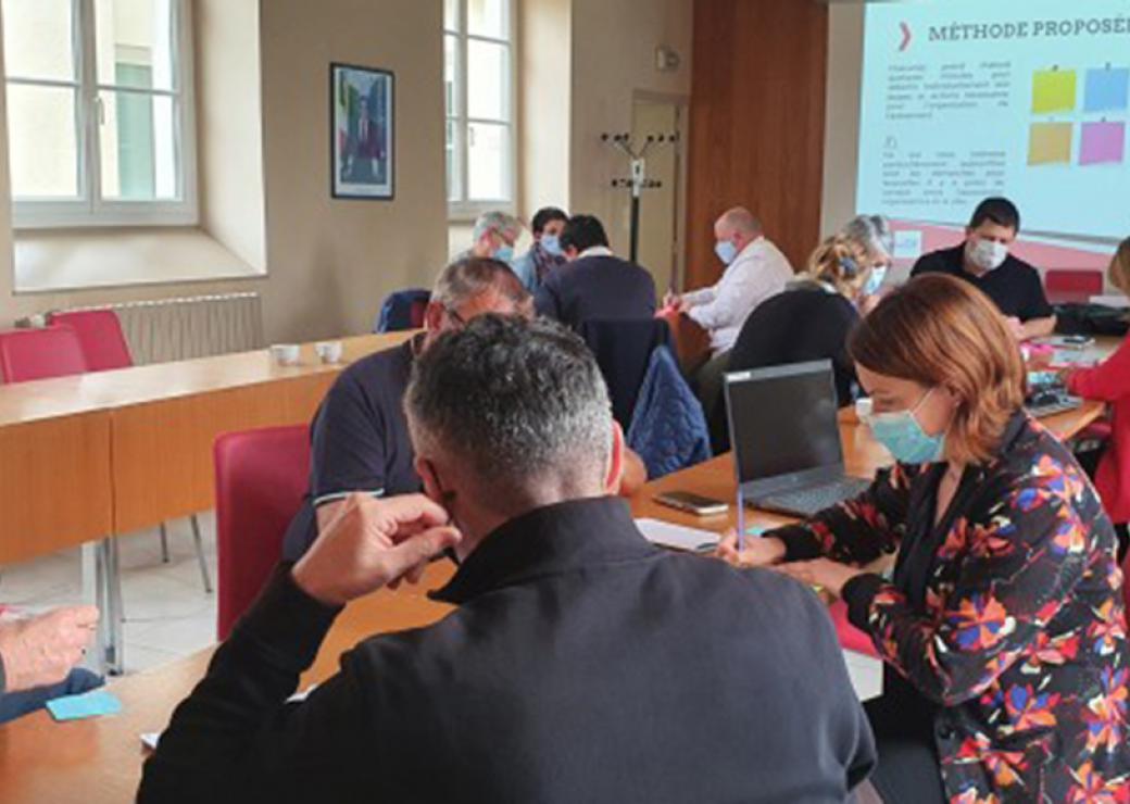 Dans une salle, une dizaine de personnes est en train de travailler par groupe de deux à quatre personnes