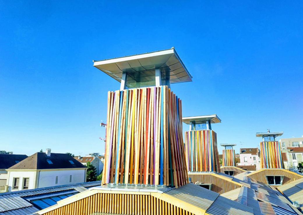 Vue sur les toits d'une ville. Des tours bardées de bois multicolore émergent de l'ensemble