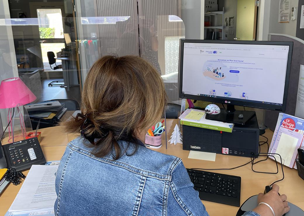 Photo d'une femme assise à un bureau, devant un écran d'ordinateur. On ne voir que son dos et son écran