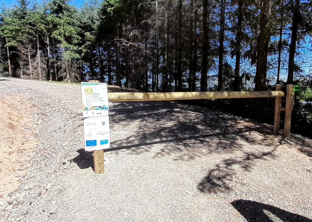 Une barrière de bois coupe l'accès à une piste bordée de résineux