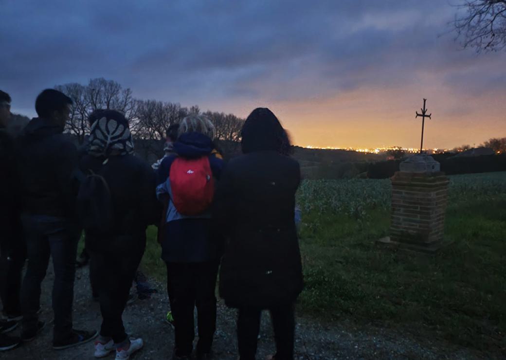 De nuit, nn groupe de 4 personnes, vues de dos, regarde en contrebas une ville éclairée