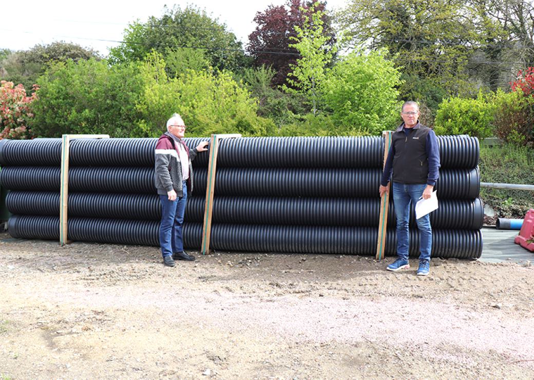 Deux hommes posent devant de très gros tuyaux de plastique noir