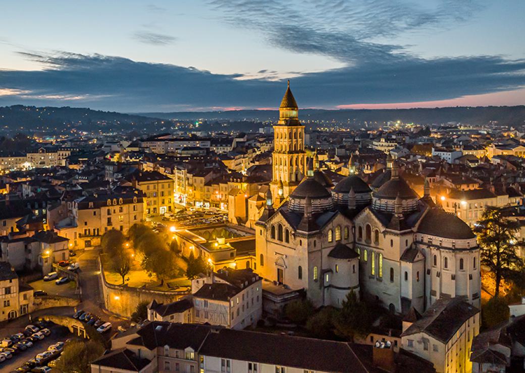 Vue aérienne entre chien et loup d'une ville. Au centre, un édifice religieux.