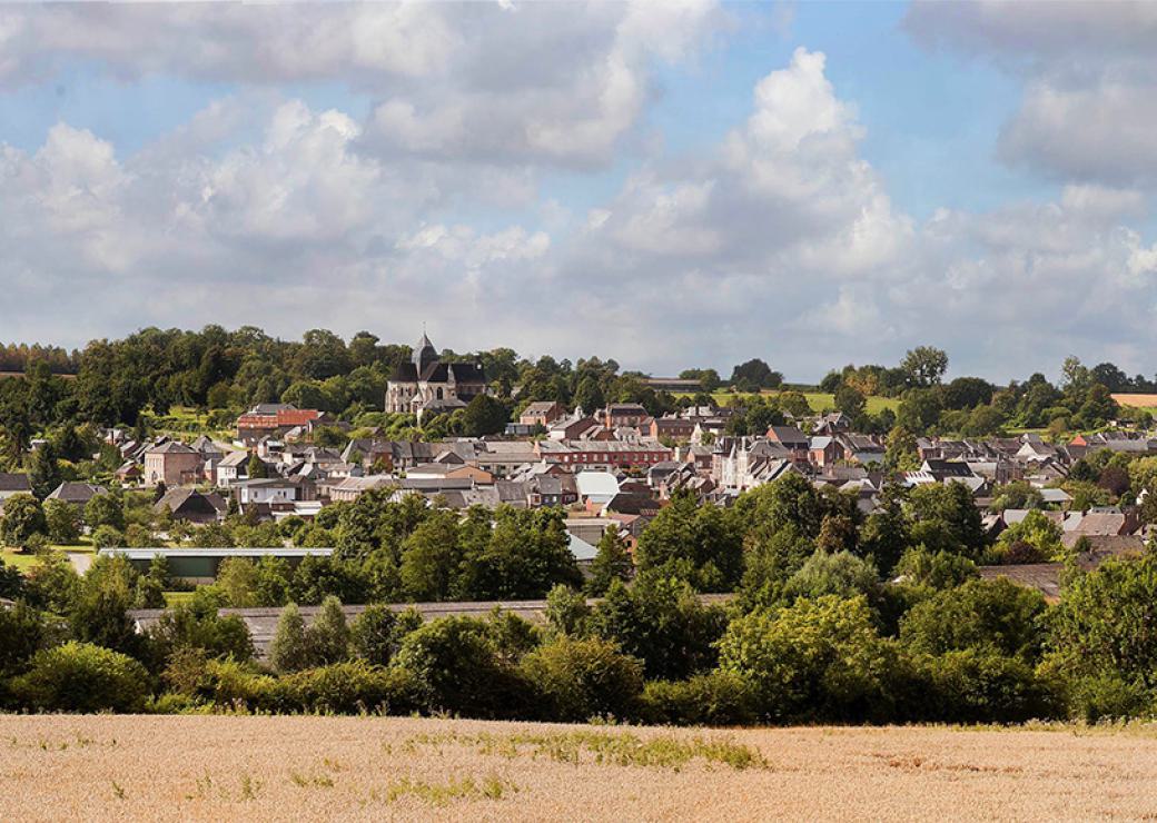 Au premier plan un champ de céréales blond, puis un village entouré d'arbres aux feuilles vertes
