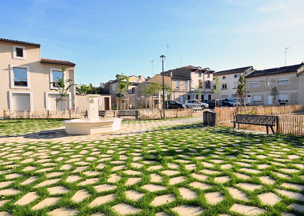 Vue d'un jardin public agrémenté d'une fontaine et de jeunes arbres tout juste plantés, au centre de maisons neuves