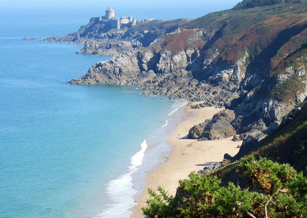 Vue aérienne d'une côte très découpée, avec des rochers plongeant dans la mer. Au fond, une citadelle.