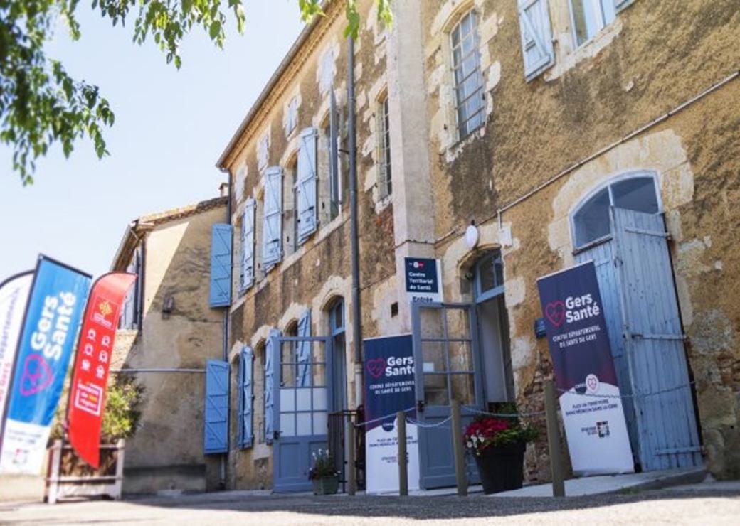 Une maison de village devant laquelle sont implantés des drapeaux où l'on peut lire "Centre de santé"