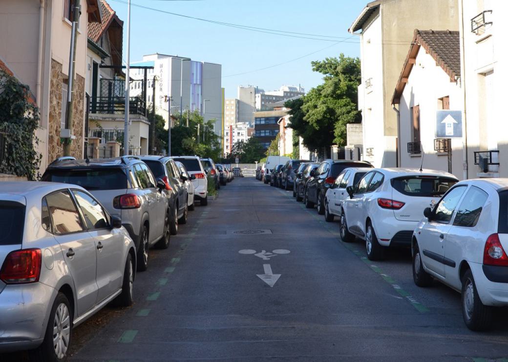 Des voitures sont garées de chaque côté d'une rue bordée de pavillons