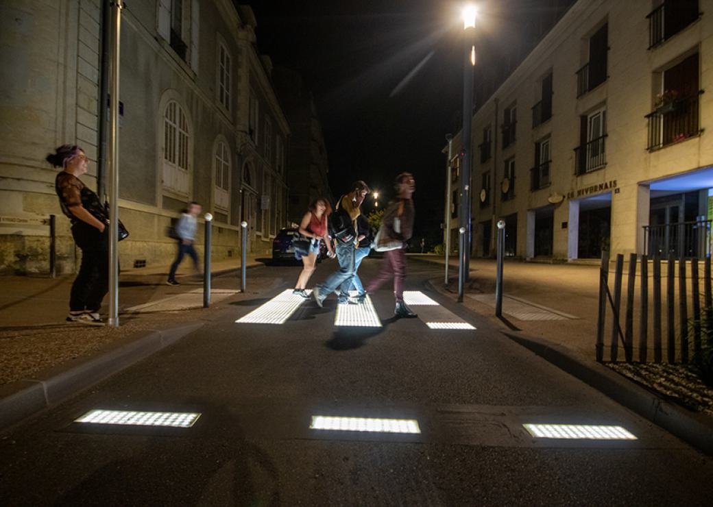 Un groupe de personnes emprunte un passage piéton. Il fait nuit et les bandes blanches émettent de la lumière