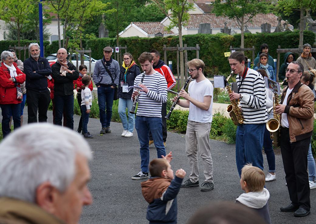 4 musiciens jouent des instruments à vent dans la rue. Des personnes les entourent, des enfants semblent danser devant eux.