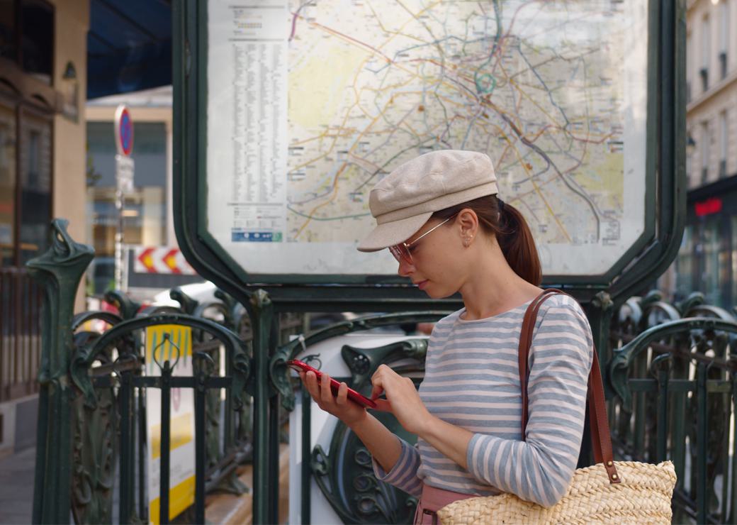 Une touriste en train de regarder son smartphone devant une entrée de métro
