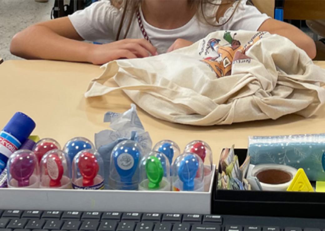 Sur le bureau d'un écolier, un sac de toile et des pots de gouache de couleur