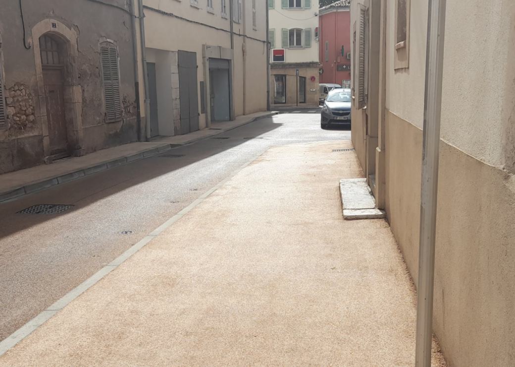 Une rue en plein soleil. Le bitume du trottoir est couleur ocre