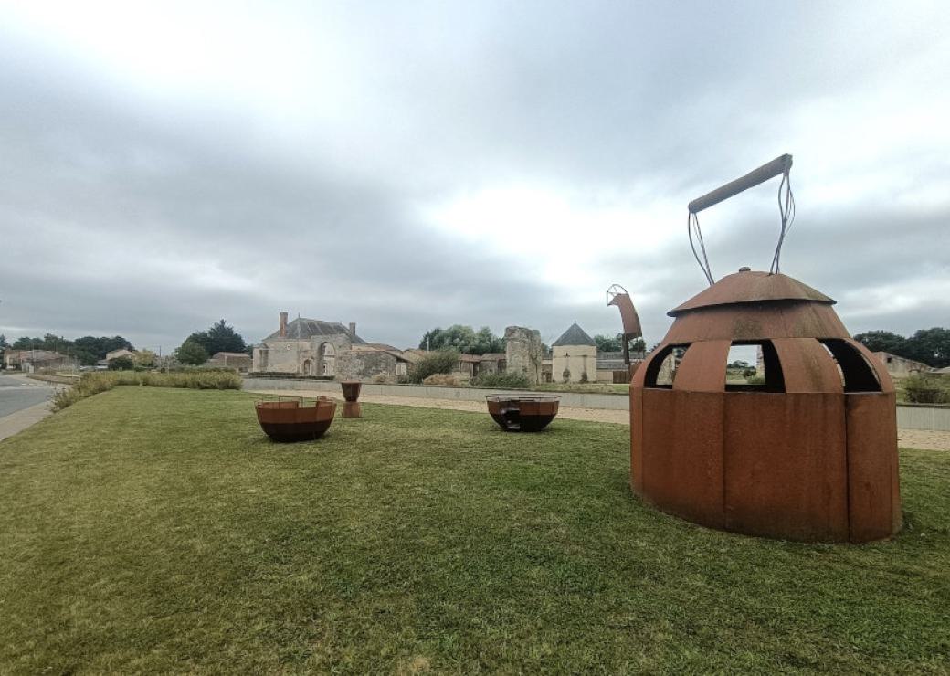 Une théière géante en métal sur une pelouse, au loin, un château