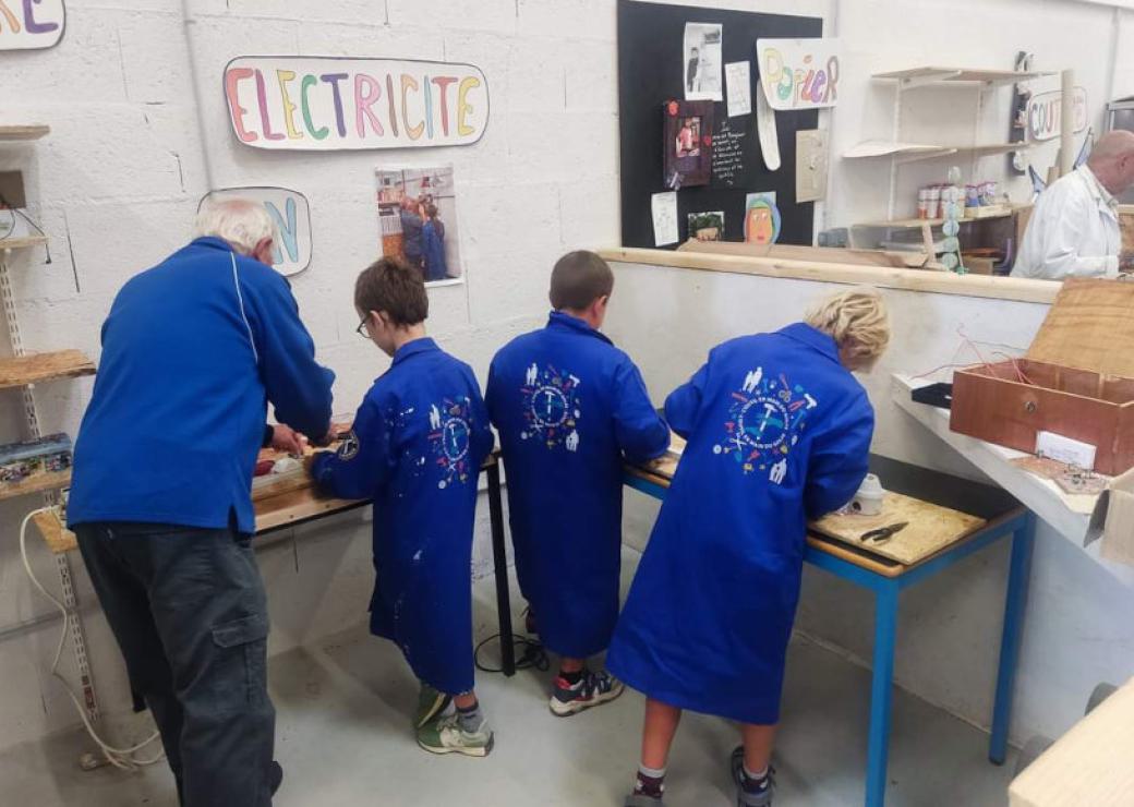 Quatre personnes en blouse bleue dans un atelier, parmi eux trois enfants