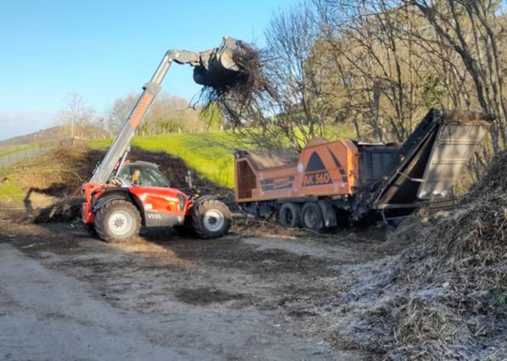Un tracto pelle charge une benne avec des branches d'arbre