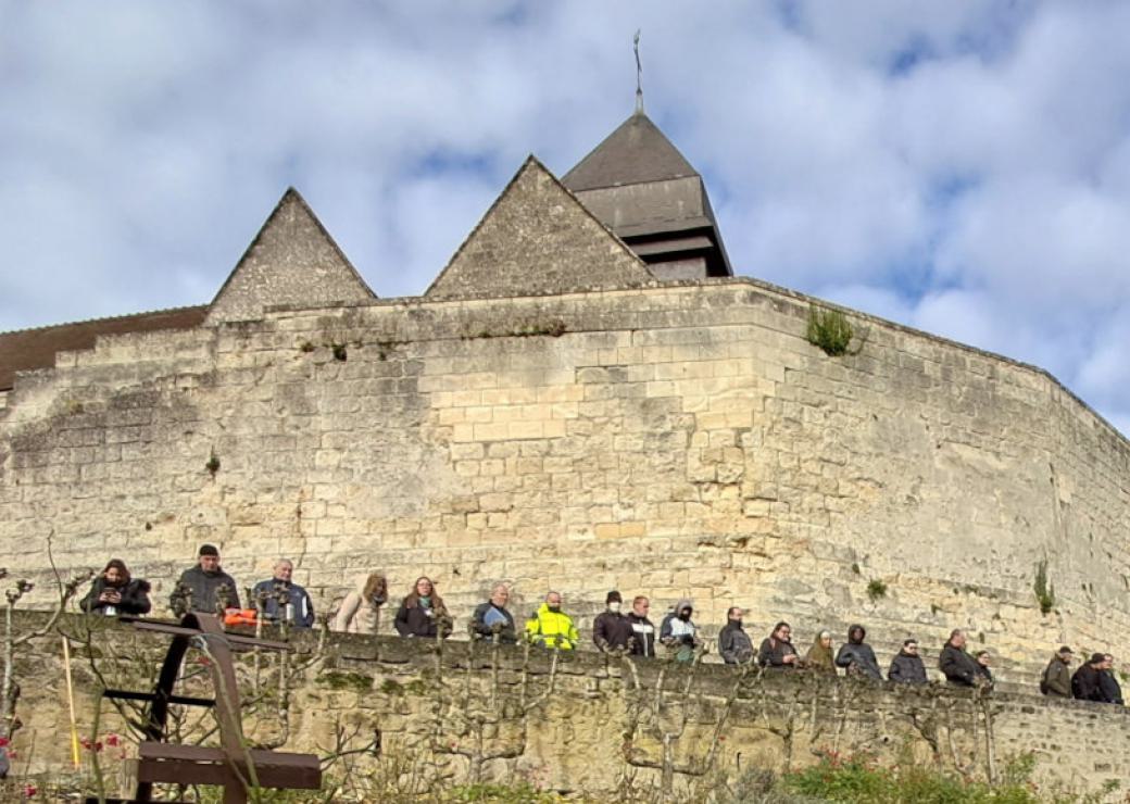 Au pied du mur d'enceinte d'un château, des personnes se tiennent contre un muret
