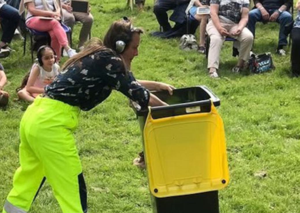 Une personne pousse une poubelle à couvercle jaune devant d'autres personnes assises