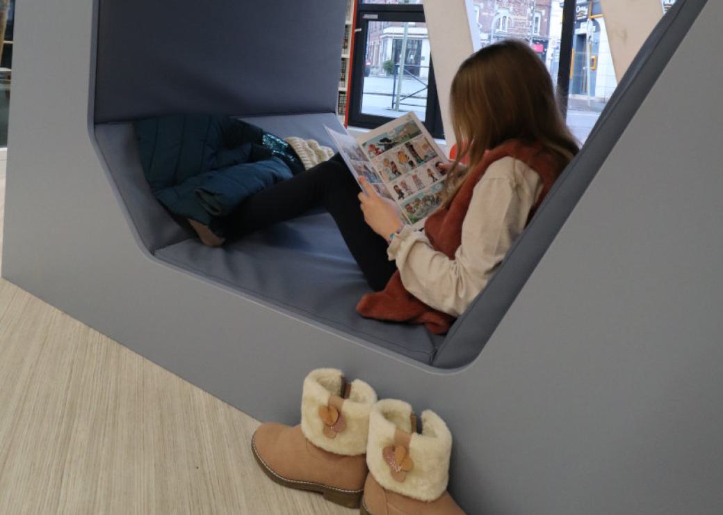 Une enfant lit une bande dessinée, installée dans une banquette en forme d'alvéole