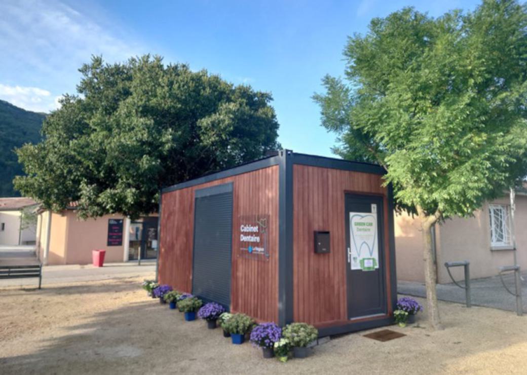 Un batiment rectangulaire type conteneur décoré, installé sur une place et entouré de fleurs en pot