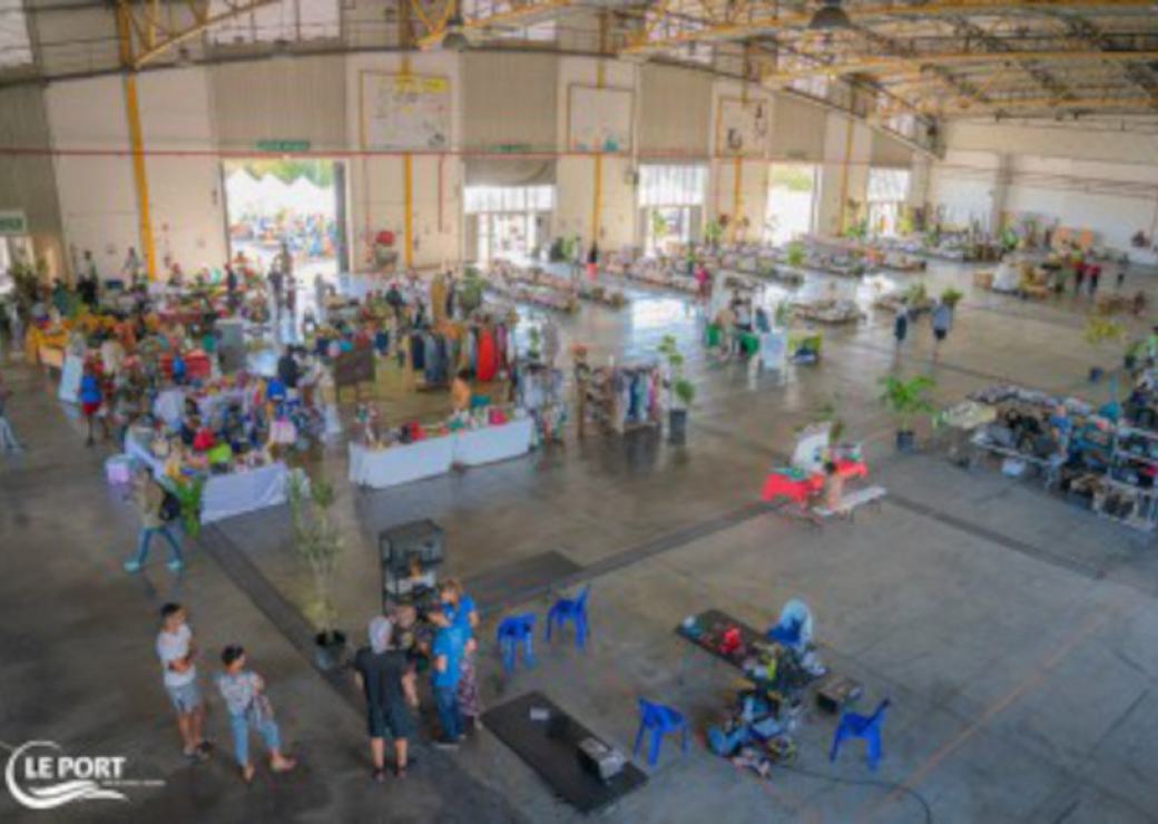 Dans une vaste halle, des stands sont installés et des gens se promènent