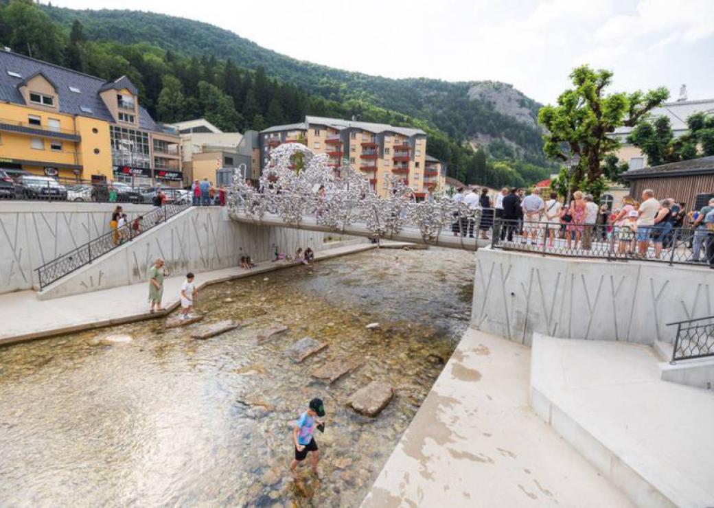 Vue d'un cours d'eau surmonté d'une passerelle, avec des personnes auprès de la passerelle et un enfant qui marche dans le cours d'eau
