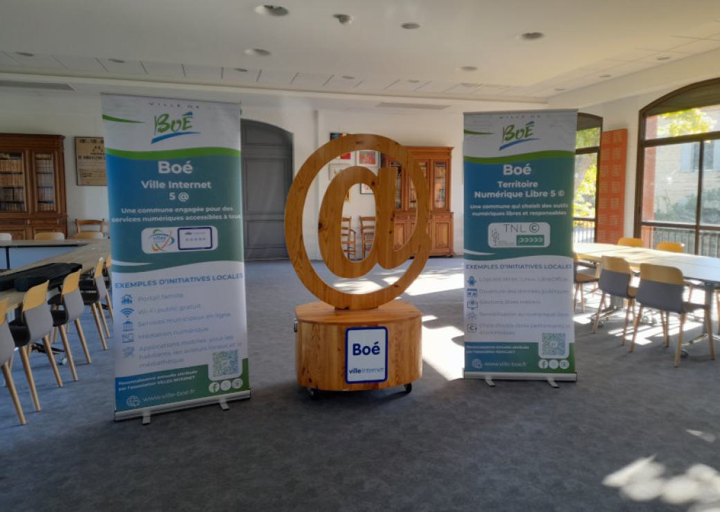 Un grand signe arobase en sculpture, entouré de deux panneaux, dans une salle type salle de réunion