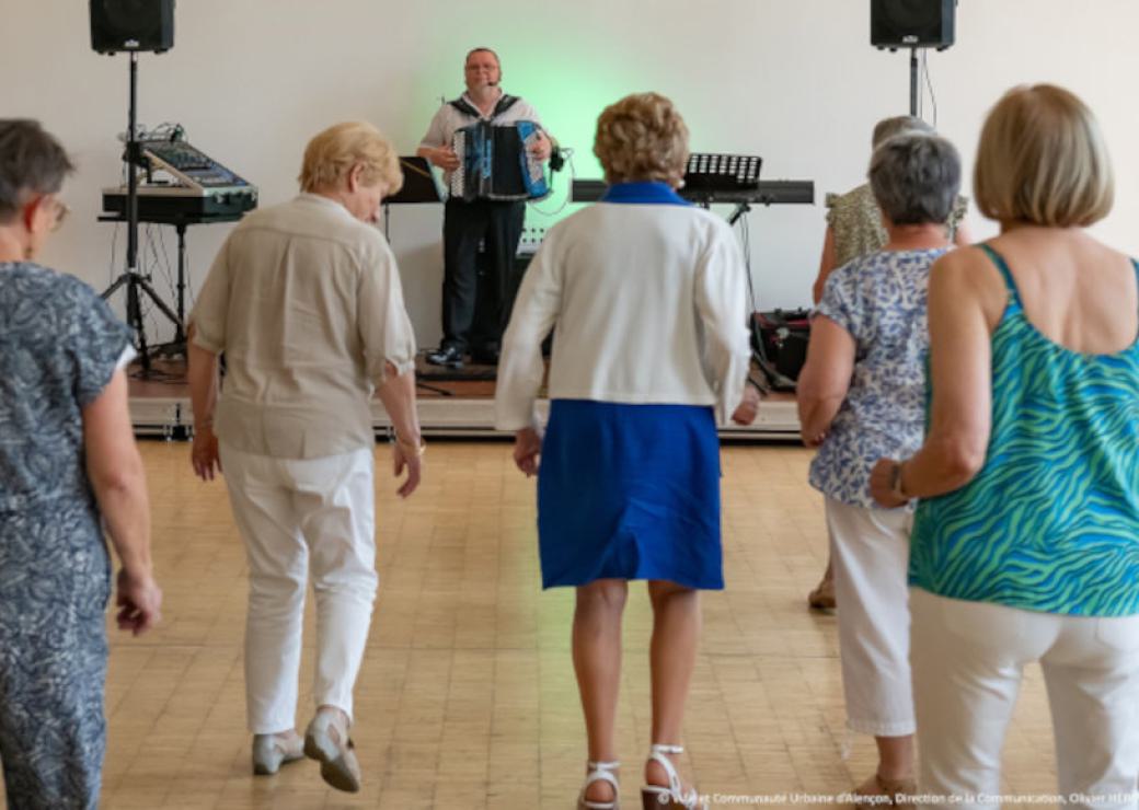 Au premier plan, des personnes dansent face à un monsieur qui joue de l'accordéon