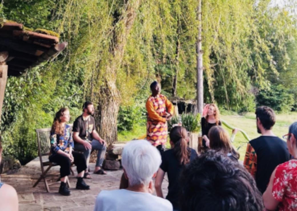 Vue d'un spectacle en plein air, depuis les spectateurs: quatre personnes font face au publics, sous un arbre