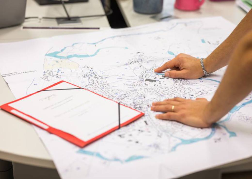 Un plan déplié sur une table, les mains d'une personne sur ce plan