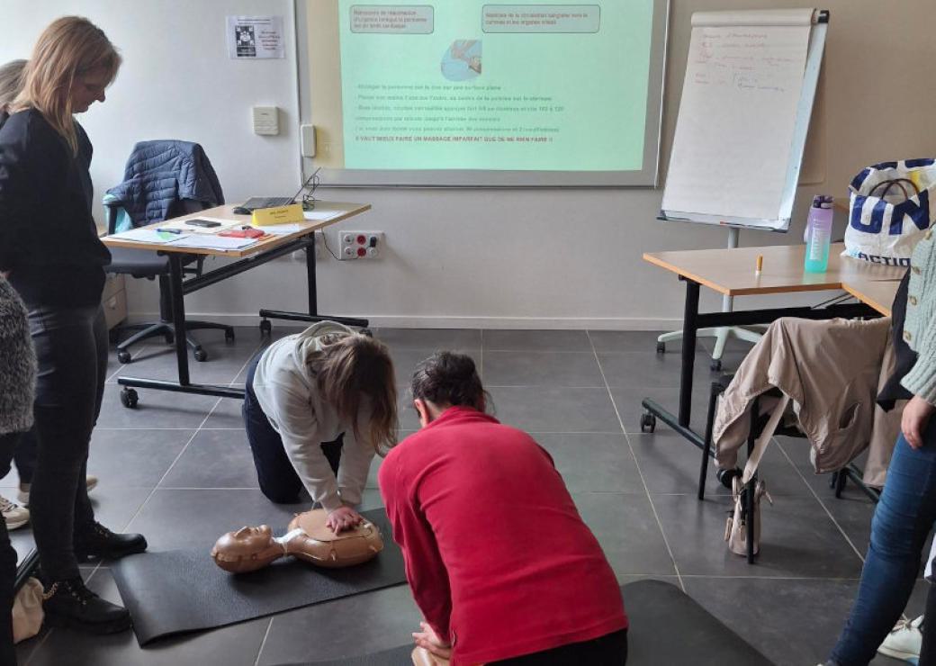 Des personnes pratique un massage cardiaque sur un mannequin au sol
